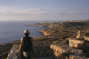 Traveler overlooking the Gozo coastline from a scenic viewpoint with Mediterranean landscape and soft evening light.
