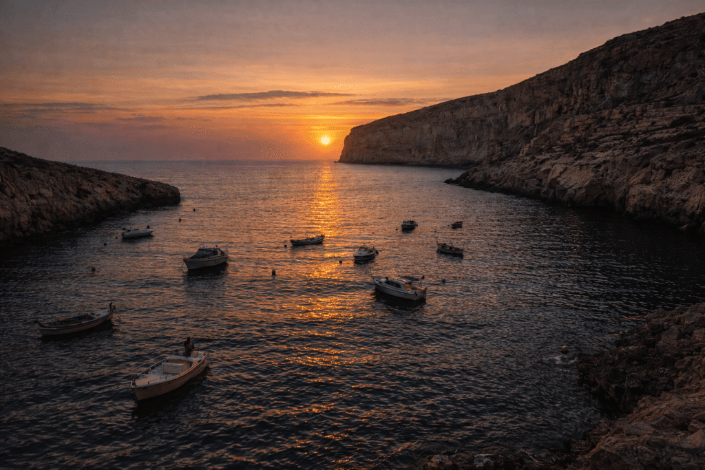 Xlendi Bay sunset in Gozo with boats and warm reflections on the water Description: Evening light reflecting across Xlendi Bay, with boats in calm water and soft illumination from the waterfront