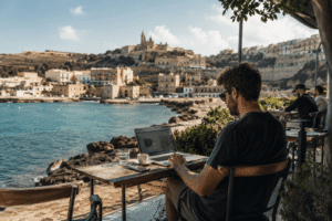 Remote worker using a laptop at a quiet seaside café in Gozo with Mediterranean coastal views
