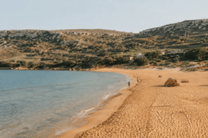 Golden sandy beach in Gozo with clear Mediterranean water, limestone hills, and warm natural sunlight.
