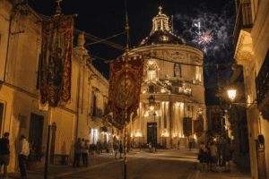 Evening festa atmosphere in Xewkija, Gozo with illuminated church façade, festa banners, and warm village street lighting.