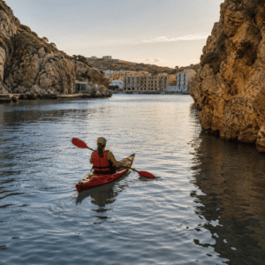 Kayak on calm water inside Xlendi Bay with limestone cliffs and waterfront buildings.