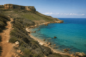 Remote red sand beach at San Blas Bay in Gozo, Malta surrounded by rugged cliffs and Mediterranean vegetation.